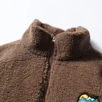 Флісова куртка кавового та бежевого кольорів із високим коміром і нашивкою на грудях.
